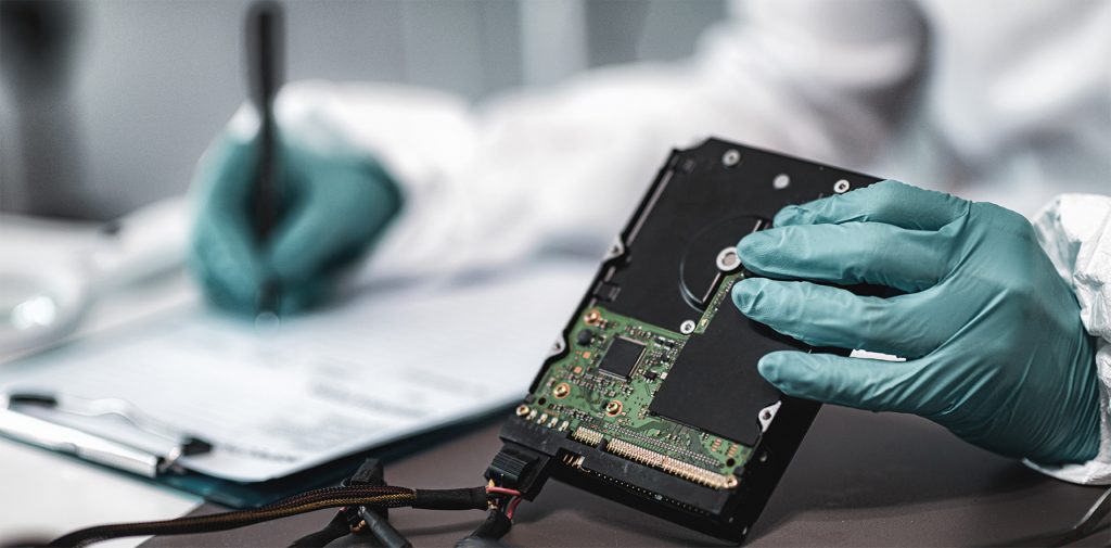 Gloved hands handling an exposed hard drive during a compliance and risk mitigation procedure