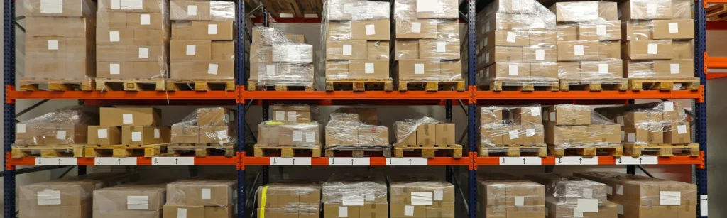 Warehouse shelves filled with packaged boxes on pallets, representing fulfillment center storage and pricing factors